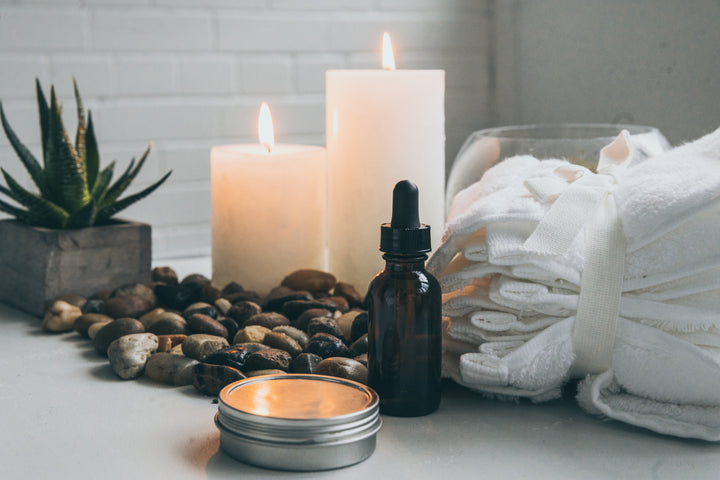 Honey & CoCo, Rejuvenate face Serum on countertop in front of towels, rocks and candles. 